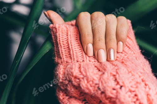 Preview: Pretty nude color manicure, one finger shiny golden, on knitted pink wool pillover background