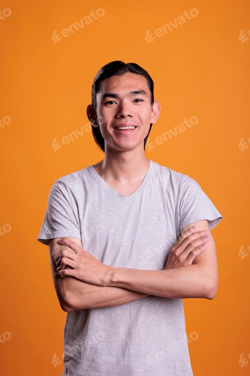 Preview: Young smiling happy asian man standing with arms crossed