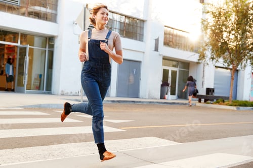 Preview: Fashionable young Hispanic woman in dungarees running across the street, full length, close up