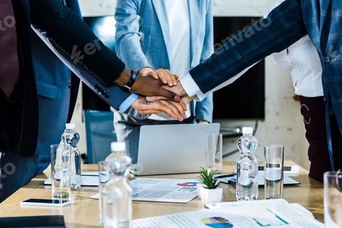 Preview: cropped view of multicultural men and women putting hands together near charts and graphs