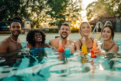 Preview: Happy friends enjoying refreshing drinks in swimming pool at sunset