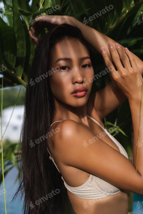 Preview: Beautiful asian thai woman with soft smooth clean dark tanned skin posing by palm leaves