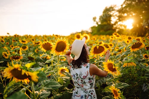 Preview: Beautiful woman posing in a field of sunflowers in a dress and hat. Fashion, lifestyle concept.