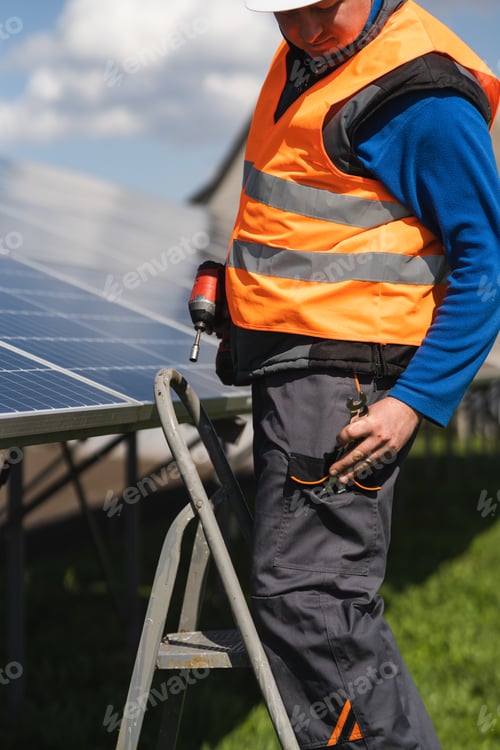 Preview: Male engineer who installs and maintains solar panels stands on a stepladder