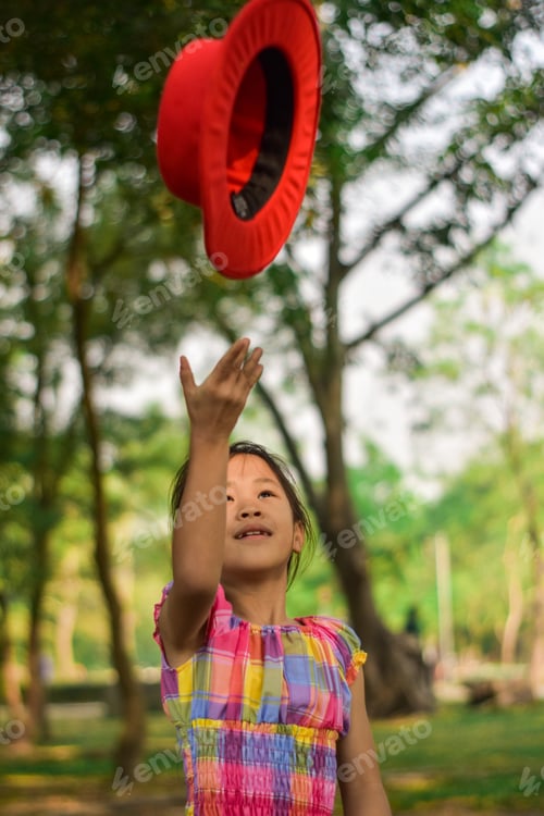 Preview: Cute little girl throwing a red hat in a summer green park.