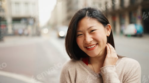 Preview: Cheerful Asian woman looking at camera smiling standing on the city street. Happy emotions