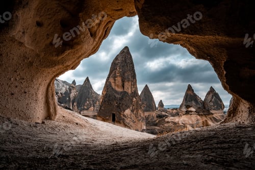 Preview: a cave filled with brown rock formations near mountains and clouds
