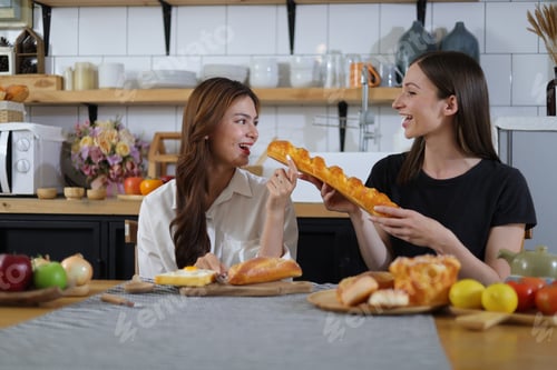 Preview: Two happy young women in the kitchen practice baking bread and tasting.