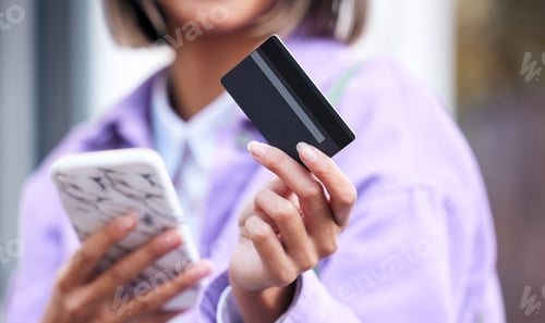 Preview: Shot of an unrecognizable woman using her cellphone and credit card while out shopping in the city