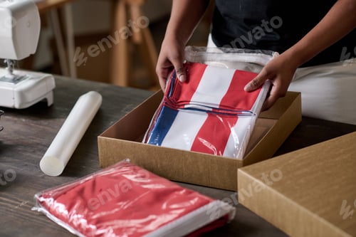 Preview: Hands of young black woman putting folded handmade USA flag into box