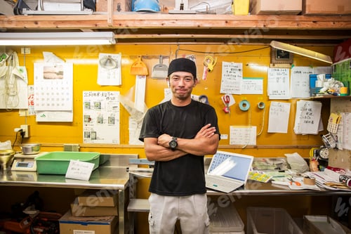 Preview: Japanese farmer wearing black cap standing in his office, smiling at camera.