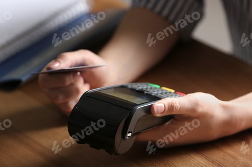 Preview: Woman using modern payment terminal at table indoors, closeup