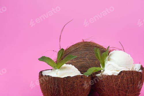 Preview: Vanilla ice cream balls in fresh coconut halves decorated with mint leaves on a pink background