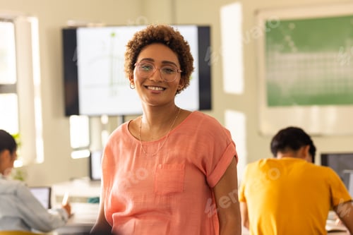 Preview: Smiling teacher in classroom with students working on laptops in high school