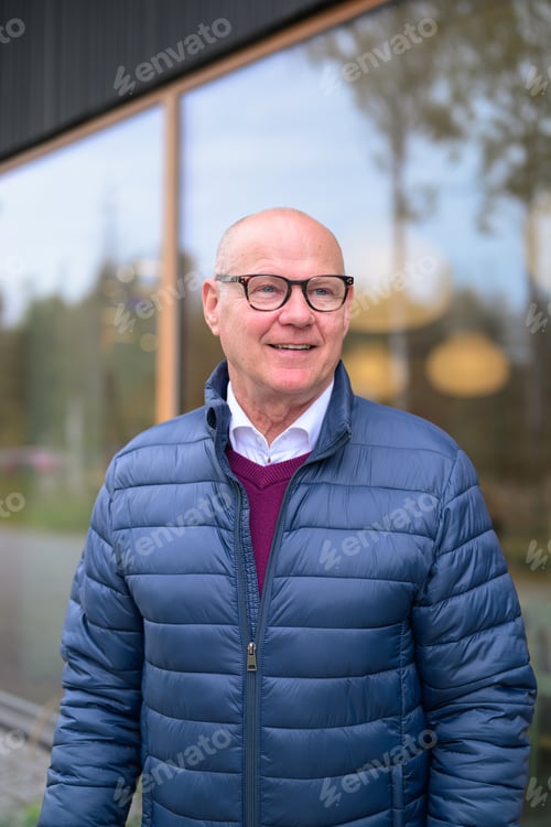 Preview: Portrait of a happy senior man in a blue jacket with glasses in city