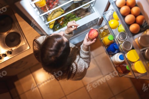 Preview: Woman eating an apple in front of an open fridge