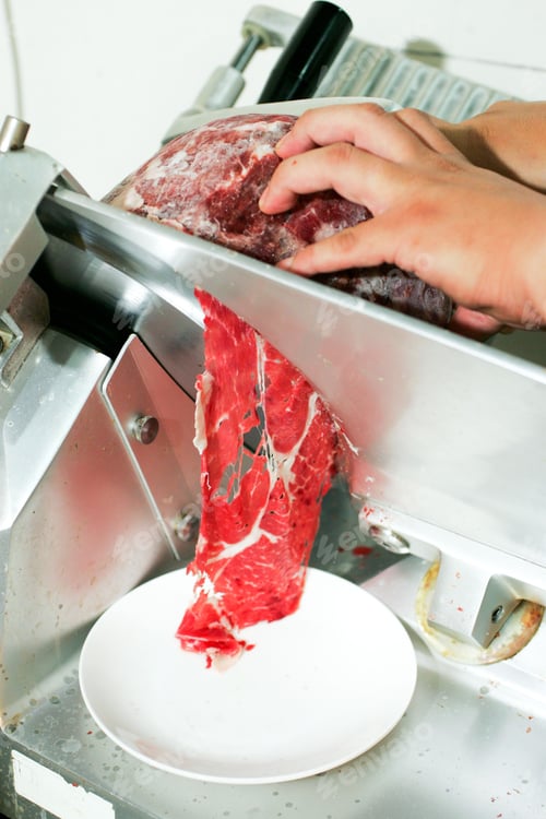 Preview: Close-up of hands slicing raw meat with a meat slicer in a kitchen setting