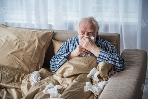 Preview: Sick Senior Man Suffering From Illness. He Is Sitting In Bed Covered With Blanket And Blowing His