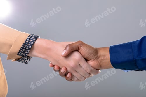 Preview: Midsection of caucasian and african american business people shaking hands on grey background