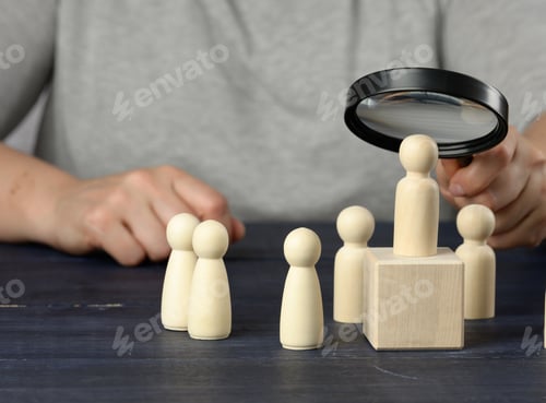 Preview: Hand with a magnifying glass examines unique and talented wooden men in the crowd