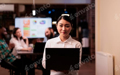 Preview: Portrait of smiling asian office worker holding laptop in business office during late night meeting