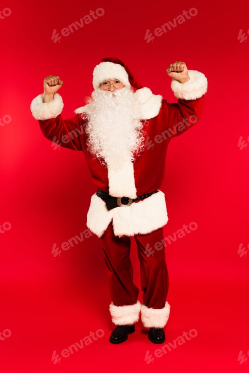 Preview: Bearded father christmas in eyeglasses showing yes gesture at camera on red background