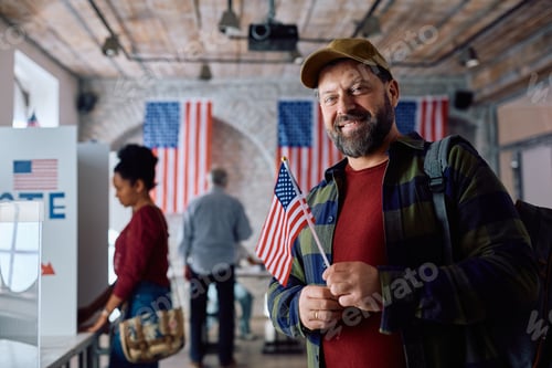 Preview: Happy mature man with USA flag at the polling place looking at camera.