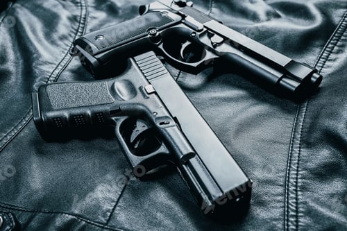 Preview: Two handguns placed on a black leather background in a dimly lit space
