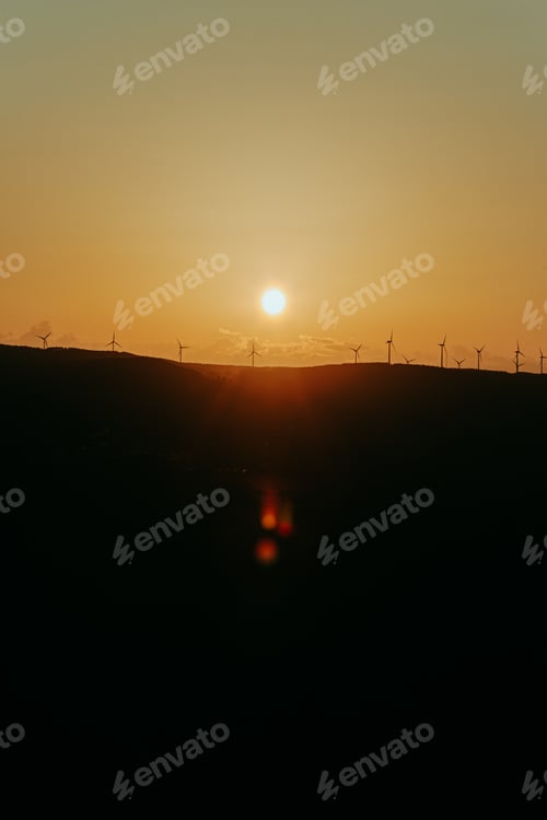 Preview: Silhouettes of some wind mills on the top of a mountain during a super orange sunset