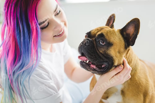Preview: attractive girl with colorful hair petting and looking at cute french bulldog