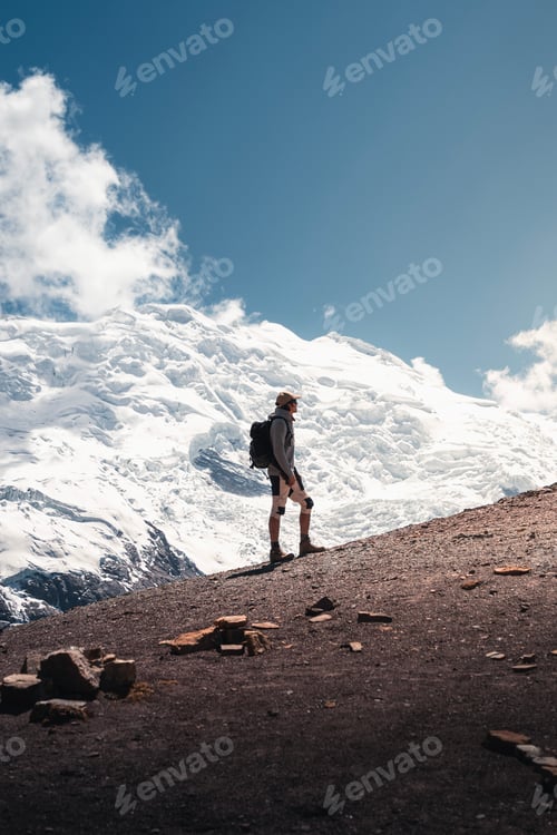 Preview: Hiker contemplating majestic snowy mountain peak under blue sky