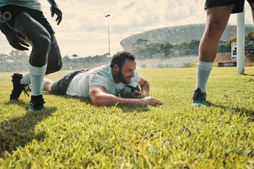 Preview: Cropped shot of a handsome young rugby player scoring a try while training on a rainy day