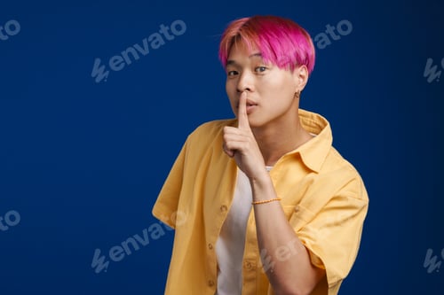 Preview: Asian boy with pink hair showing silence gesture at camera