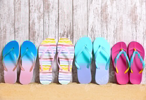 Preview: Different bright flip flops on sand near wooden wall, space for text. Summer beach accessories