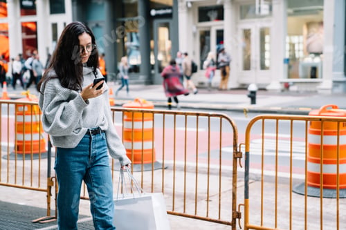 Preview: Young woman walking down street and browsing mobile phone