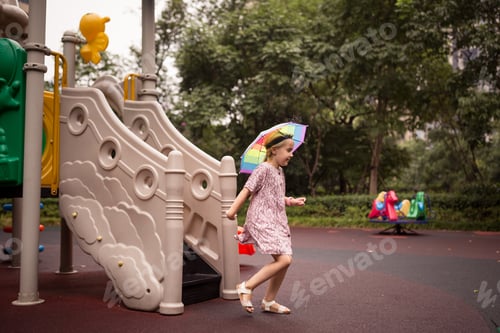 Preview: Child playing at playground. Little girl six years old wearing head umbrella because was rainy day