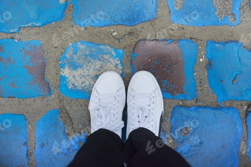 Preview: Legs of woman in white sneakers on vintage blue painted pavers