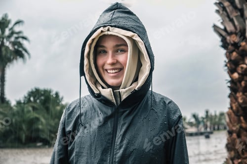 Preview: Portrait of a smiling young woman in a raincoat during a storm, hurricane, downpour on the island ag
