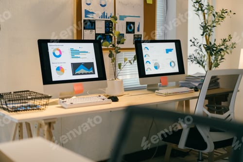 Preview: Two desktop computers are displaying financial data and charts on a desk in a modern office, suggest