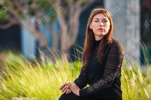 Preview: Caucasian middle-aged adult woman sitting on park bench in tropical of Dubai at gold hour