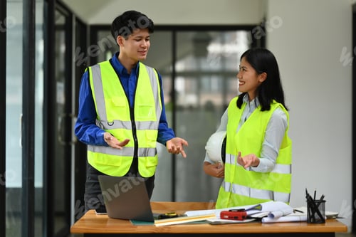 Preview: Asian male civil engineer in yellow vests discussing the new project with colleague at office.