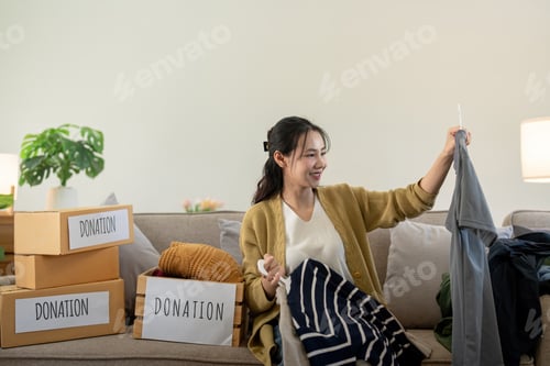 Preview: Woman asian holding donation box full with clothes and select clothes. Concept of donation and