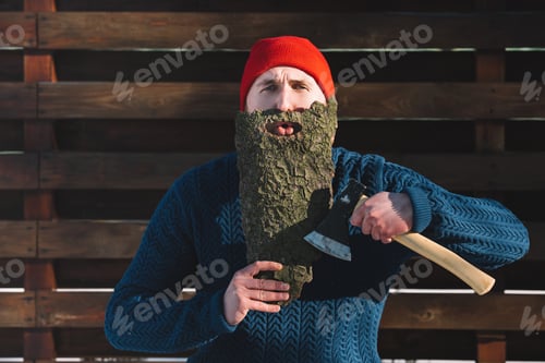 Preview: portrait of man with beard made of wood bark and axe in hand looking at camera outdoors