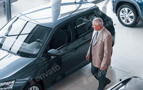 Preview: Aged man in formal wear walking in the automobile salon and looking for the car