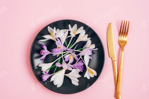 Preview: Crocus flowers on black plate and fork and knife on pink background. Diet concept. Top view, flat