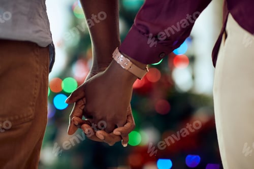 Preview: Close-up f black couple holding hands in front of Christmas tree at home.
