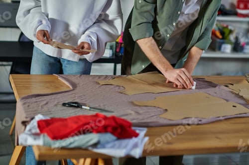 Preview: Cropped view of african american craftswoman holding sewing pattern while colleague marking fabric