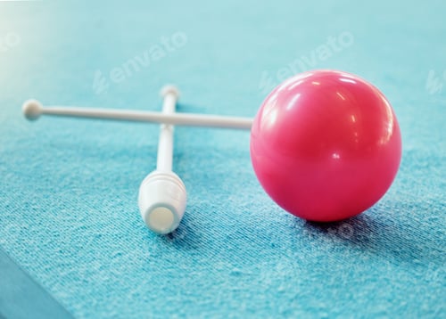 Preview: A red ball on the floor on a blue carpet. A set of drum sticks on a blue carpet next to a red spher