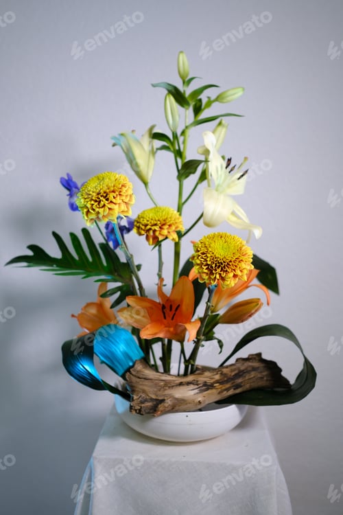 Preview: Bright floral arrangement with diverse flowers in a white vase on a simple backdrop,