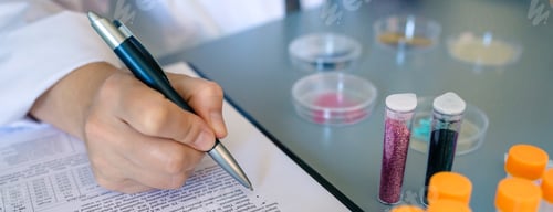 Preview: Female scientist hand filling investigation form of small plastic particles on glitter composition